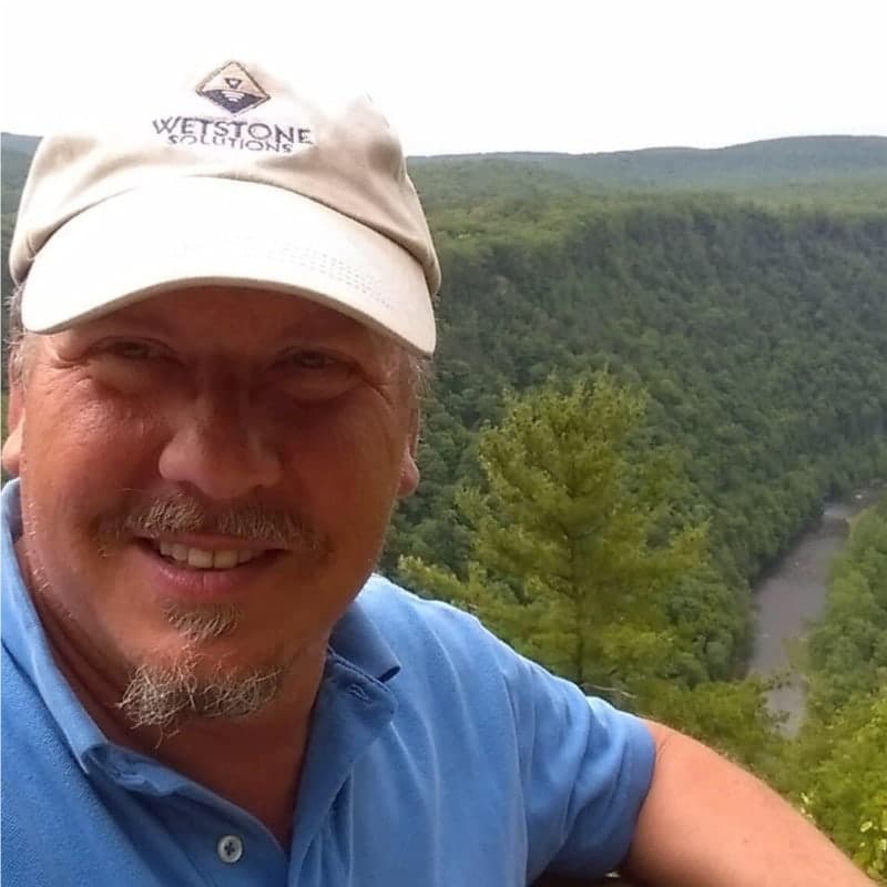 Daniel S. Fisher, P.G. in a Wetstone Solutions cap at an overlook above a forested river gorge